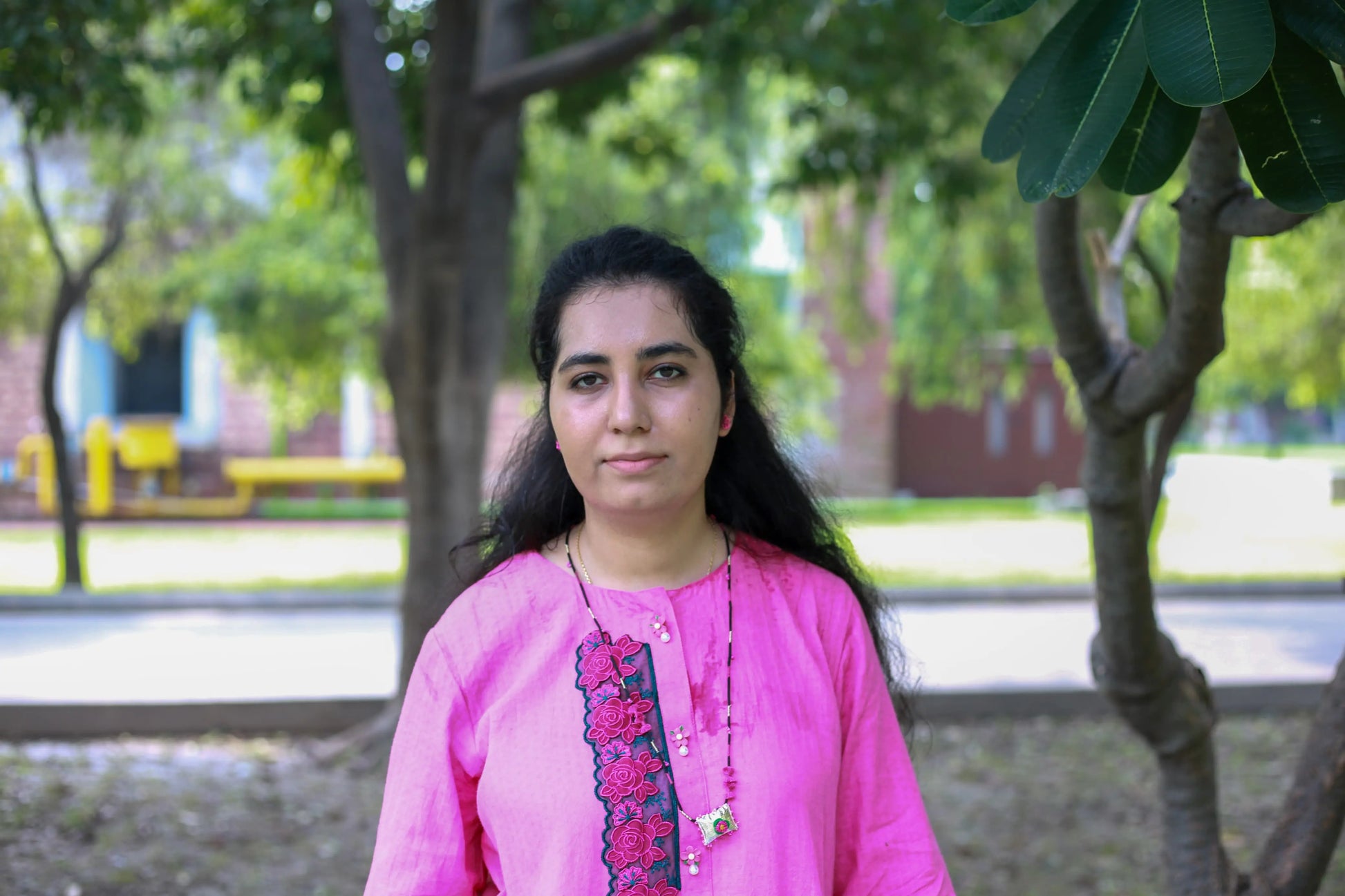 Woman in a pink traditional outfit standing outdoors with greenery in the background